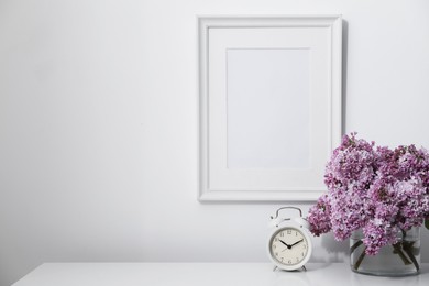 Photo of Beautiful lilac flowers and alarm clock on table near white wall indoors, space for text