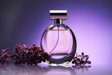Photo of Beautiful lilac flowers and perfume on mirror surface against purple gradient background