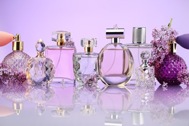 Photo of Bottles of perfume and lilac flowers on mirror surface against violet background