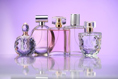 Photo of Bottles of perfume on mirror surface against violet background