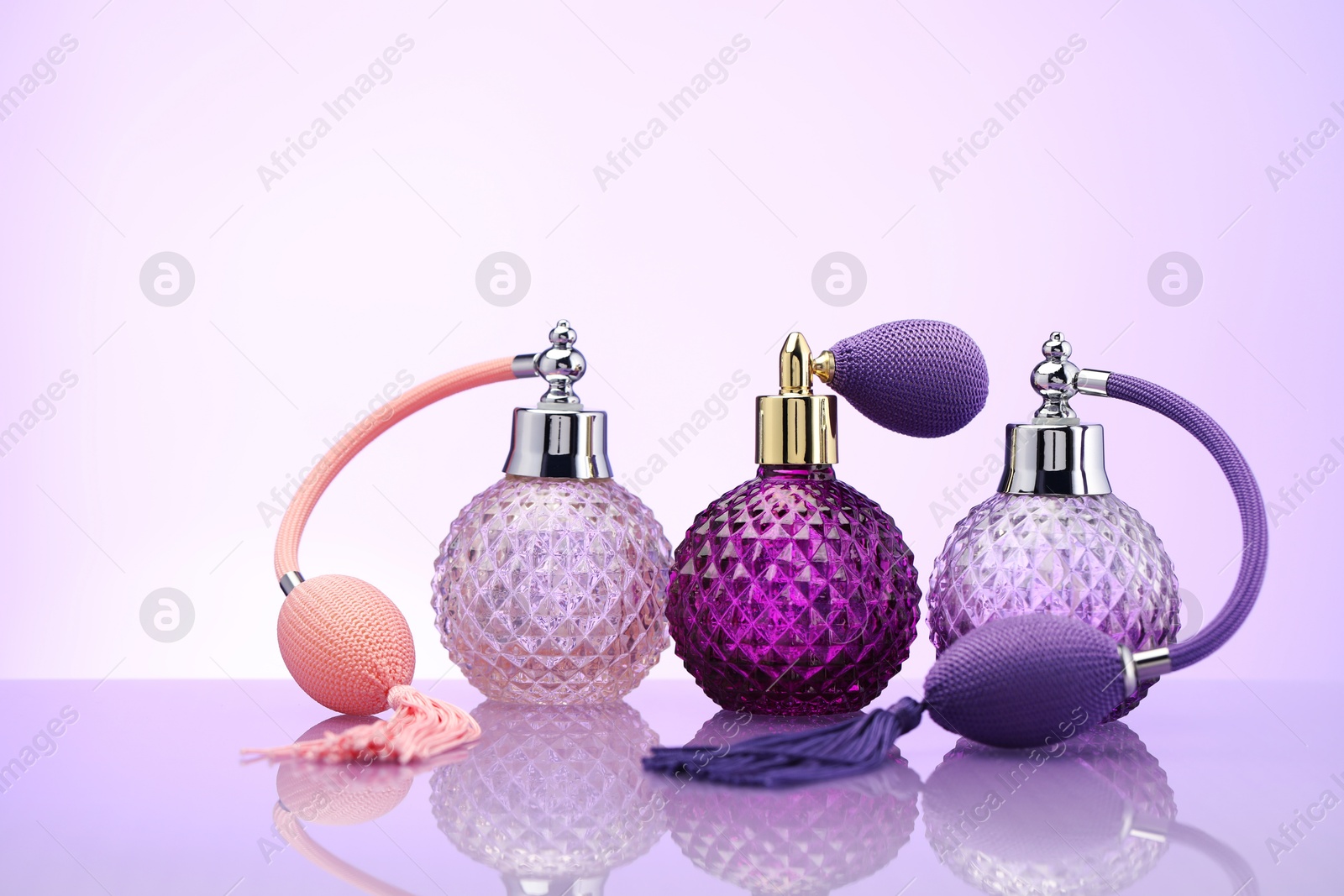 Bottles of perfume on mirror surface against pale violet gradient background Photo of Bottles of perfume on mirror surface against pale violet gradient background