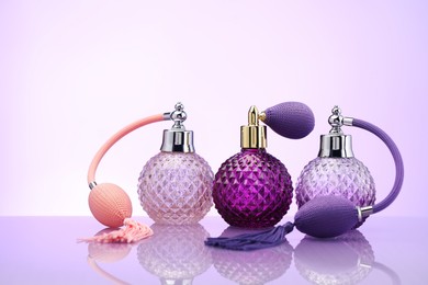 Photo of Bottles of perfume on mirror surface against pale violet gradient background