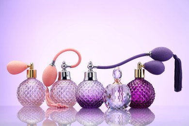 Photo of Bottles of perfume on mirror surface against pale violet gradient background