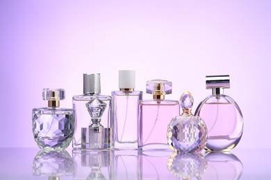 Photo of Bottles of perfume on mirror surface against pale violet gradient background