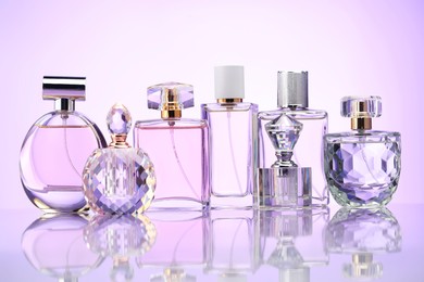 Photo of Bottles of perfume on mirror surface against pale violet gradient background