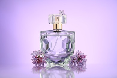 Photo of Beautiful lilac flowers and perfume on mirror surface against violet gradient background