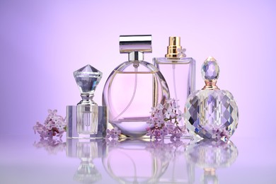 Photo of Bottles of perfume and lilac flowers on mirror surface against violet gradient background