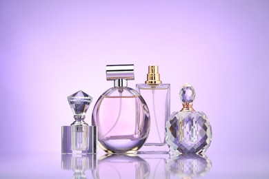 Photo of Bottles of perfume on mirror surface against violet gradient background
