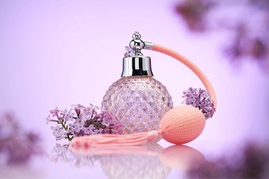 Photo of Bottle of perfume and lilac flowers on mirror surface against violet gradient background, selective focus