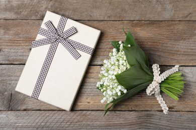Photo of Bouquet of beautiful lily-of-the-valley flowers and gift on wooden background, top view