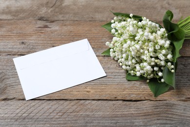 Photo of Bouquet of beautiful lily-of-the-valley flowers and envelope on wooden background, closeup