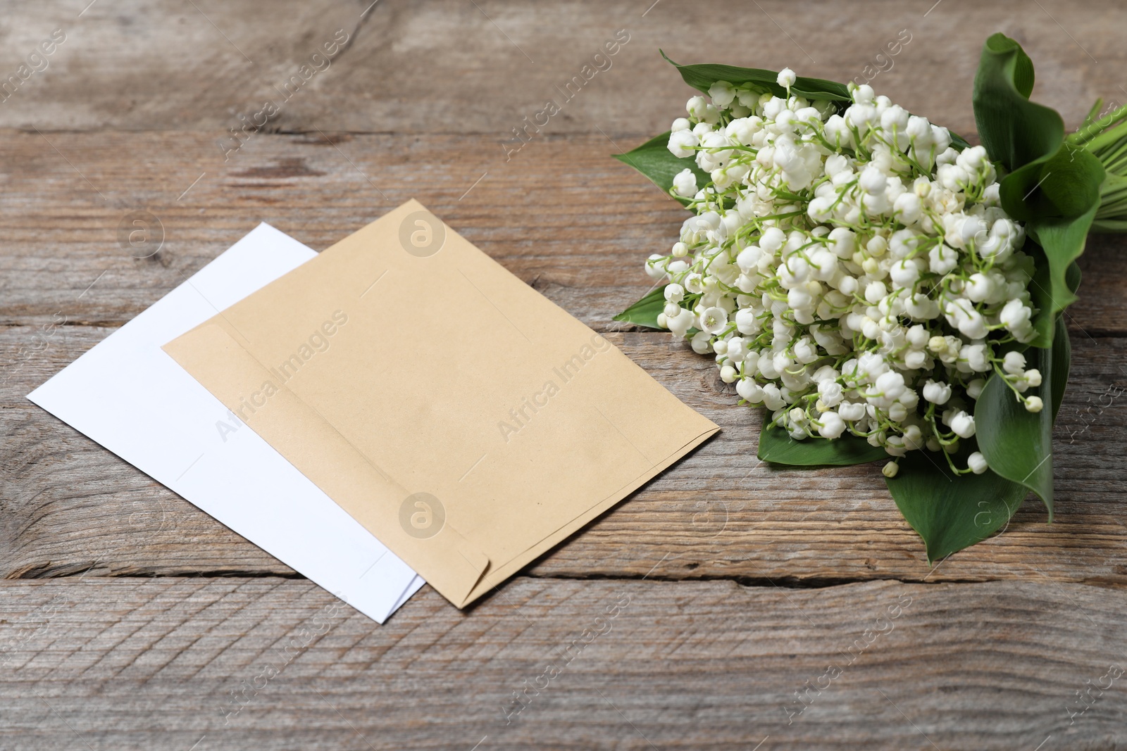 Bouquet of beautiful lily-of-the-valley flowers and envelopes on wooden background, closeup Photo of Bouquet of beautiful lily-of-the-valley flowers and envelopes on wooden background, closeup