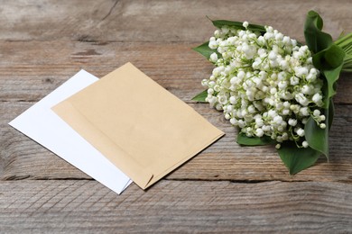 Photo of Bouquet of beautiful lily-of-the-valley flowers and envelopes on wooden background, closeup