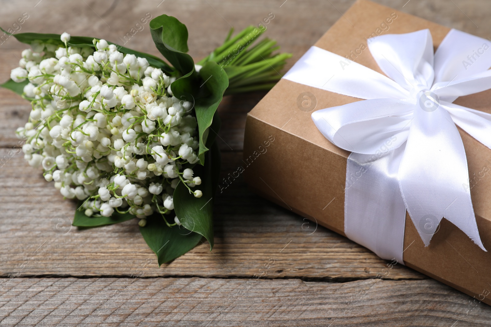 Bouquet of beautiful lily-of-the-valley flowers and gift on wooden background, closeup Photo of Bouquet of beautiful lily-of-the-valley flowers and gift on wooden background, closeup