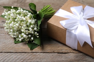 Photo of Bouquet of beautiful lily-of-the-valley flowers and gift on wooden background, closeup