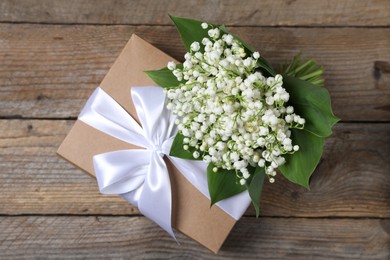 Photo of Bouquet of beautiful lily-of-the-valley flowers and gift on wooden background, top view