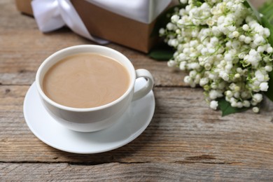 Photo of Bouquet of beautiful lily-of-the-valley flowers, coffee and gift on wooden background, closeup