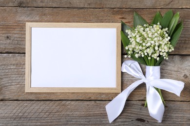 Photo of Bouquet of beautiful lily-of-the-valley flowers and blank frame on wooden background, top view. Space for text