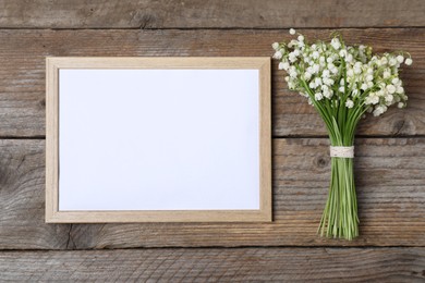 Photo of Bouquet of beautiful lily-of-the-valley flowers and blank frame on wooden background, top view. Space for text