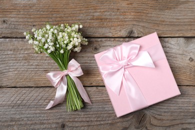 Photo of Bouquet of beautiful lily-of-the-valley flowers and gift on wooden background, top view