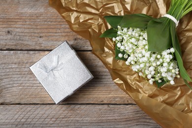 Photo of Bouquet of beautiful lily-of-the-valley flowers and gift on wooden background, top view