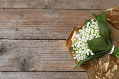 Photo of Bouquet of beautiful lily-of-the-valley flowers on wooden background, top view. Space for text