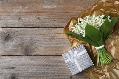 Photo of Bouquet of beautiful lily-of-the-valley flowers and gift on wooden background, top view. Space for text