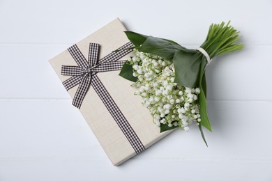 Photo of Bouquet of beautiful lily-of-the-valley flowers and gift on white wooden background, top view