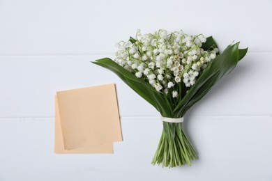 Photo of Bouquet of beautiful lily-of-the-valley flowers and notes on white wooden background, top view