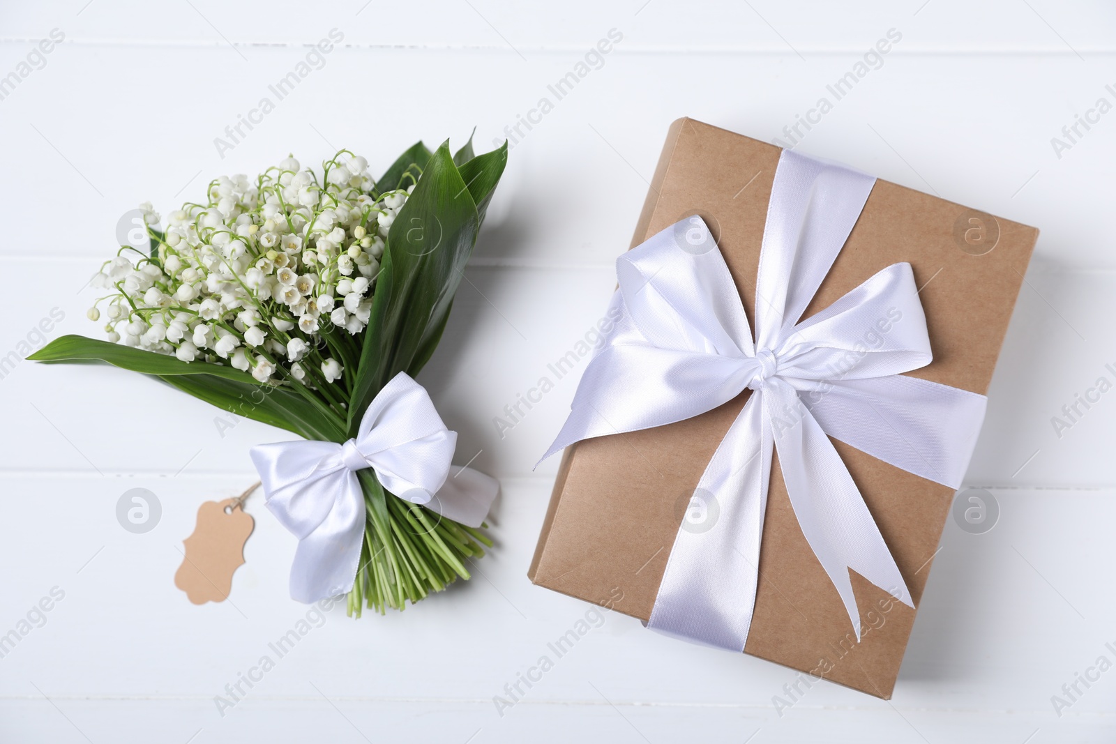 Bouquet of beautiful lily-of-the-valley flowers and gift on white wooden background, top view Photo of Bouquet of beautiful lily-of-the-valley flowers and gift on white wooden background, top view