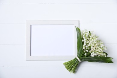 Photo of Bouquet of beautiful lily-of-the-valley flowers and blank frame on white wooden background, top view. Space for text