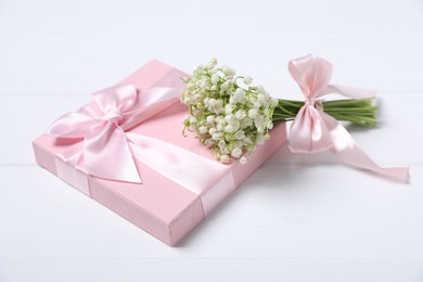 Photo of Bouquet of beautiful lily-of-the-valley flowers and gift on white wooden background, closeup