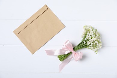 Photo of Bouquet of beautiful lily-of-the-valley flowers and envelope on white wooden background, top view