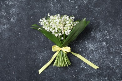 Photo of Bouquet of beautiful lily-of-the-valley flowers on black textured background, top view