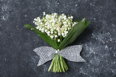 Photo of Bouquet of beautiful lily-of-the-valley flowers on black textured background, top view