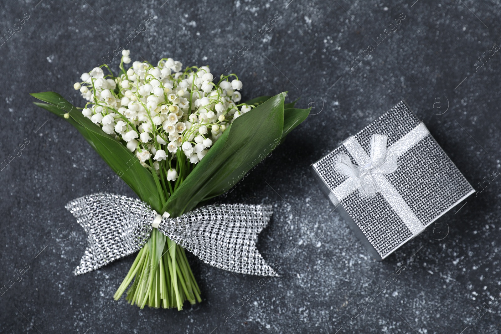 Bouquet of beautiful lily-of-the-valley flowers and gift on black textured background, top view Photo of Bouquet of beautiful lily-of-the-valley flowers and gift on black textured background, top view
