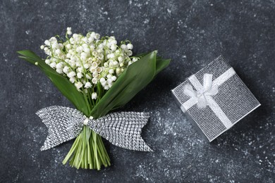 Photo of Bouquet of beautiful lily-of-the-valley flowers and gift on black textured background, top view