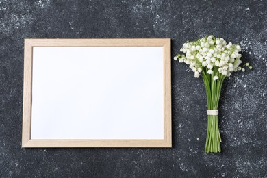Photo of Bouquet of beautiful lily-of-the-valley flowers and blank frame on black textured background, top view. Space for text