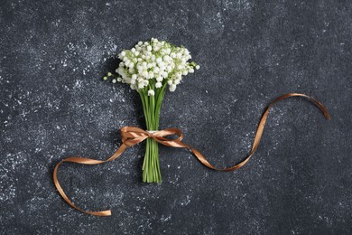 Photo of Bouquet of beautiful lily-of-the-valley flowers on black textured background, top view