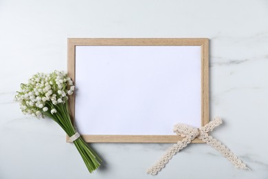 Photo of Bouquet of beautiful lily-of-the-valley flowers and blank frame on white marble background, top view. Space for text