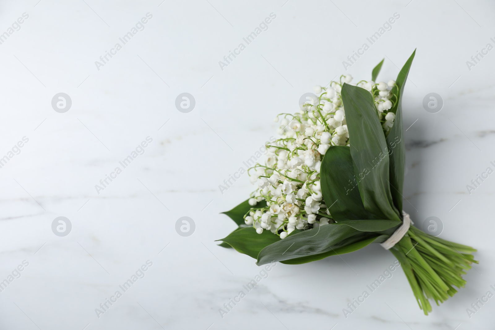 Bouquet of beautiful lily-of-the-valley flowers on white marble background, top view. Space for text Photo of Bouquet of beautiful lily-of-the-valley flowers on white marble background, top view. Space for text