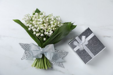 Photo of Bouquet of beautiful lily-of-the-valley flowers and gift on white marble background, top view