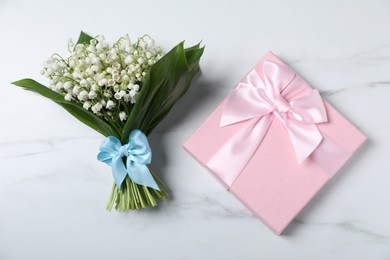 Photo of Bouquet of beautiful lily-of-the-valley flowers and gift on white marble background, top view