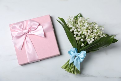 Photo of Bouquet of beautiful lily-of-the-valley flowers and gift on white marble background, top view