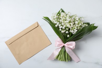 Photo of Bouquet of beautiful lily-of-the-valley flowers and envelope on white marble background, top view