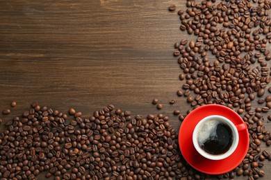 Photo of Aromatic coffee in cup and beans on wooden table, flat lay. Space for text