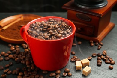 Photo of Aromatic coffee beans in cup, grinder and brown sugar on black table, closeup