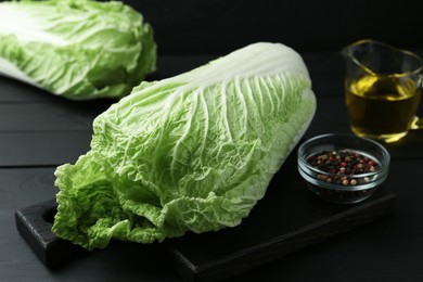 Photo of Fresh Chinese cabbages, oil and peppercorns on black wooden table, closeup