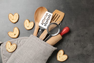 Photo of Different kitchen utensils in oven mitten and cookies on grey table, flat lay
