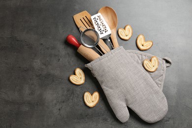 Photo of Different kitchen utensils in oven mitten and cookies on grey table, flat lay. Space for text